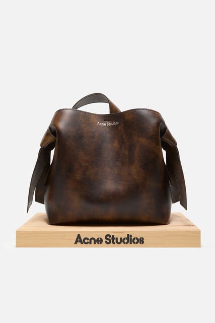 Female model showing Acne Studios black Musubi leather bag, wearing blue jeans.