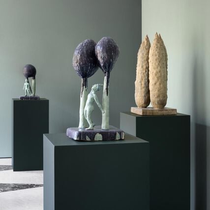 An exhibition place with green-teal background, showcasing sculptures made by Peter Schlesinger.