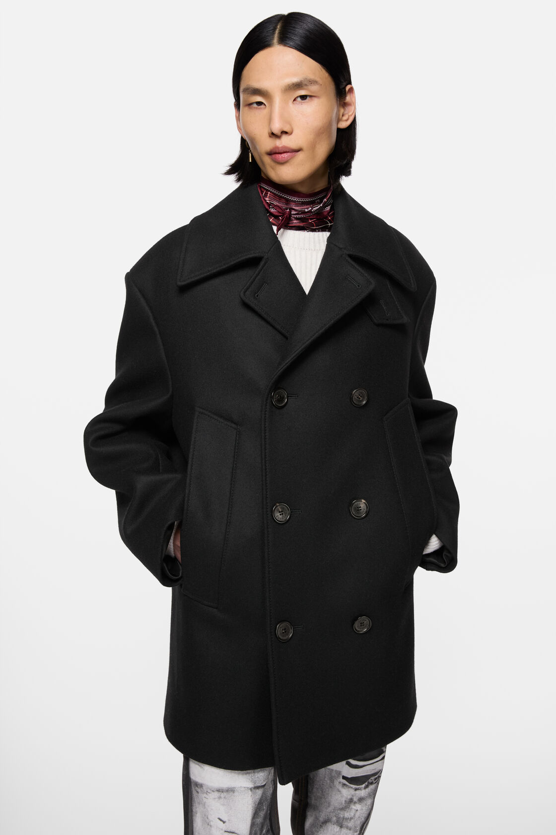 Acne Studios black wool peacoat with double-breasted button front, wide lapels, and boxy relaxed fit, styled with printed trousers and a patterned