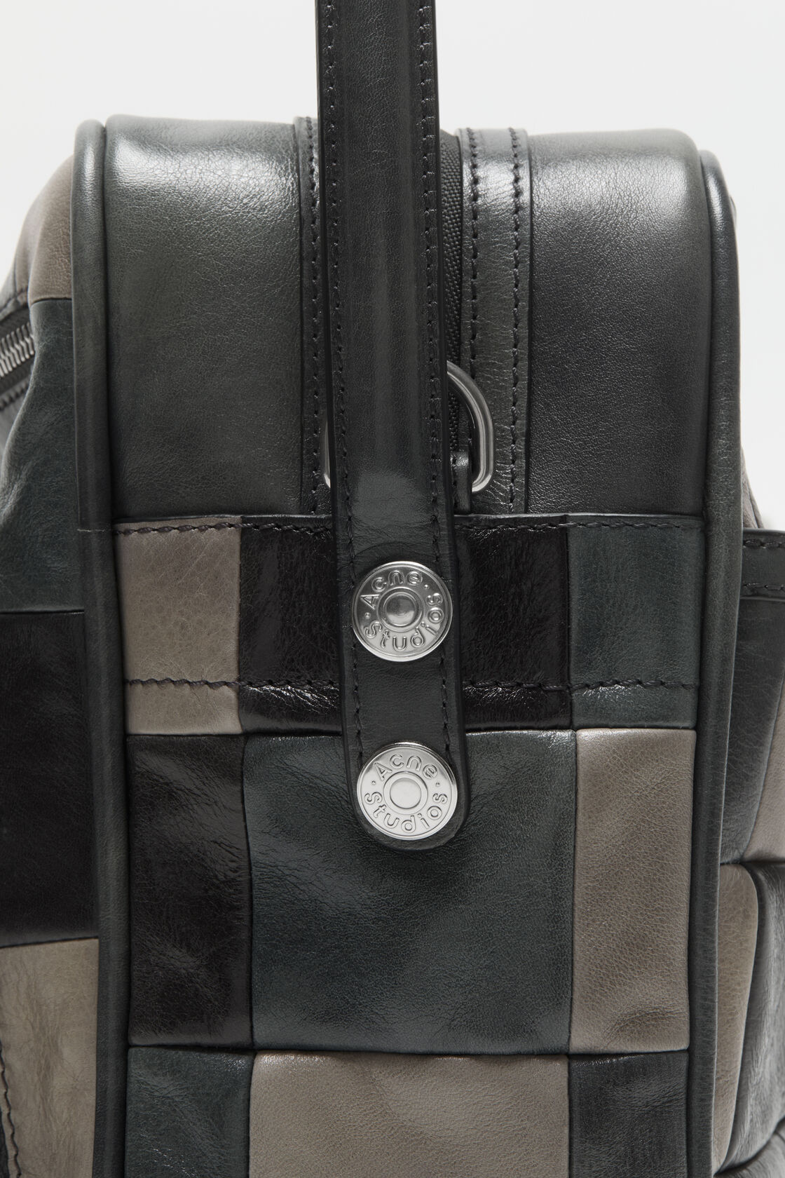 Close-up of the interior of an Acne Studios dark grey leather camera bag, showing a black branded label and monogram lining.