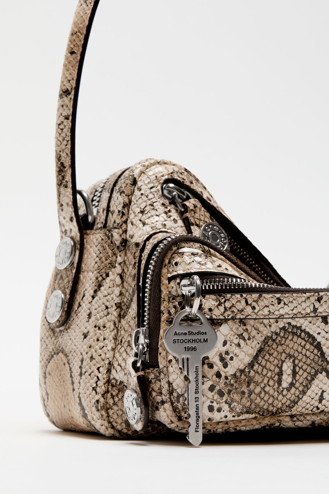 Close-up of an Acne Studios bag interior showing a dark brown leather label and black logo-jacquard lining, with beige multi snakeskin-embossed