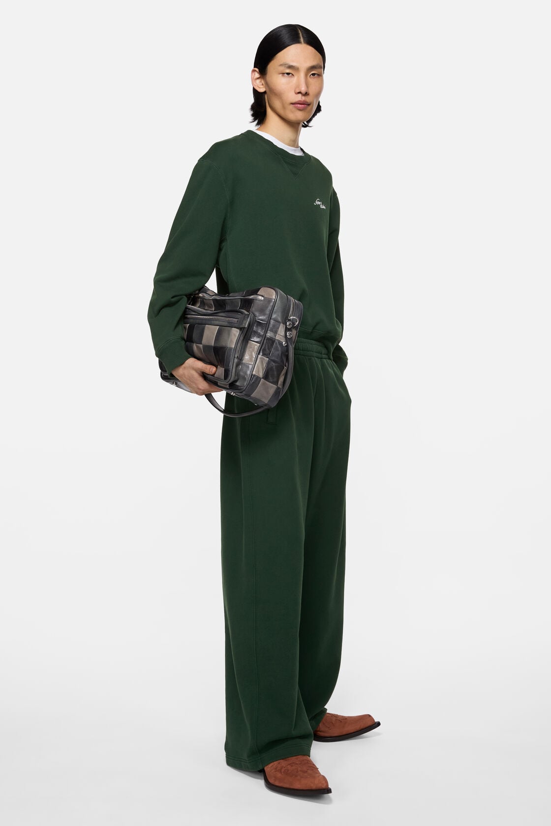 Acne Studios dark green fleece logo sweatpants in a loose, wide-leg fit, worn with a matching green sweatshirt and brown boots, styled with a plaid