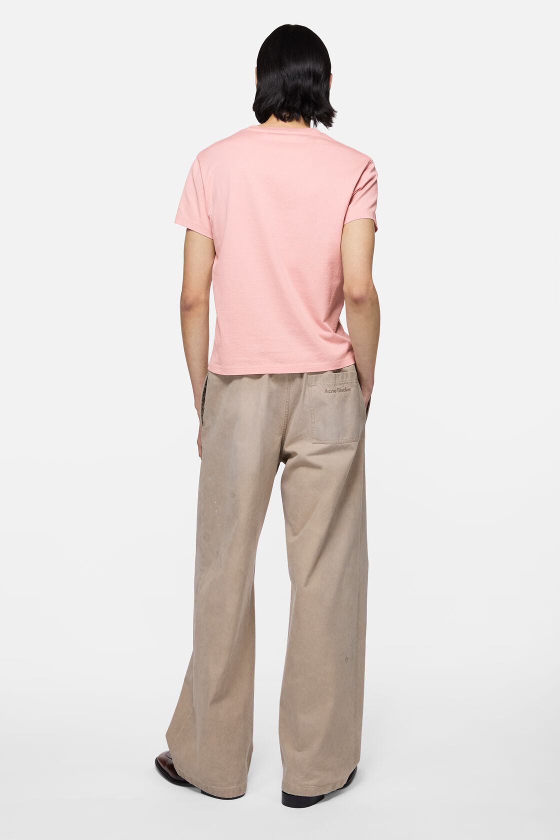 Acne Studios fitted faded pink cotton jersey t-shirt with logo, worn with wide-leg beige trousers. Rear view.