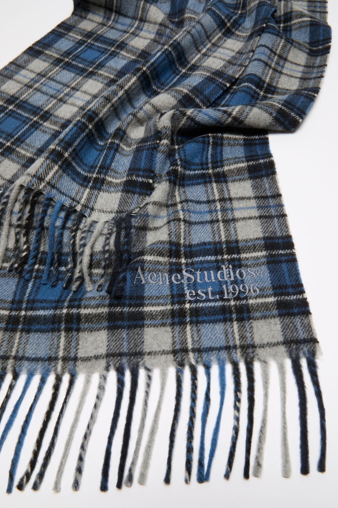 Close-up of an Acne Studios blue and grey tartan cashmere scarf with fringe ends and an embroidered logo.