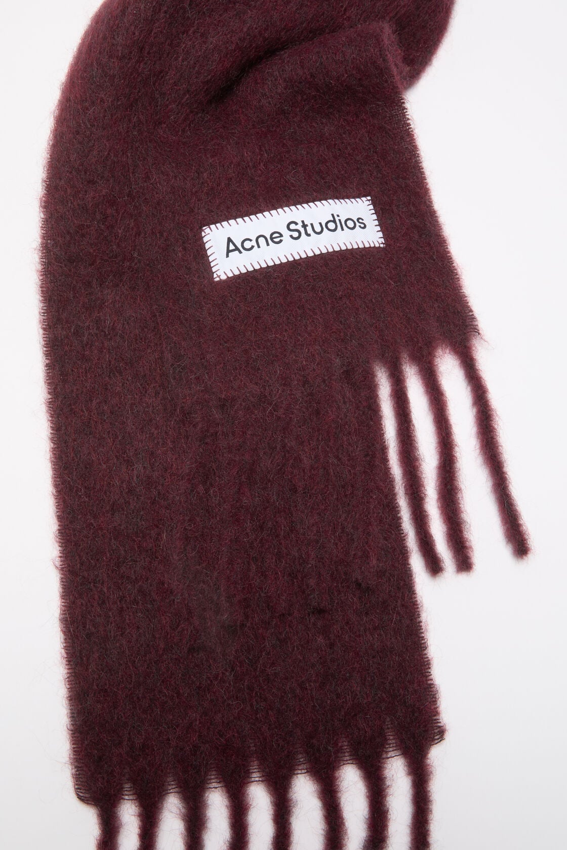Close-up of an Acne Studios skinny scarf in burgundy mohair-wool blend with a fuzzy texture and fringed ends.