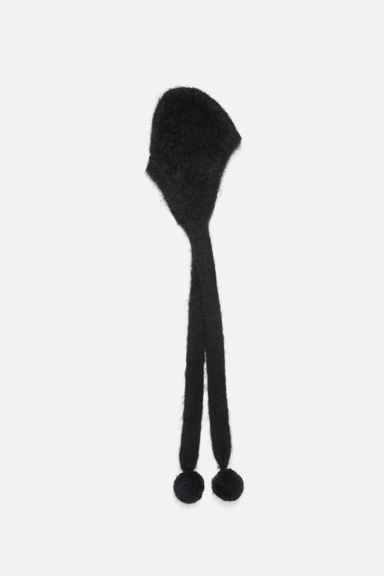 Acne Studios black mohair blend cap with earflaps and long ties ending in pom poms, shown flat on a white background.