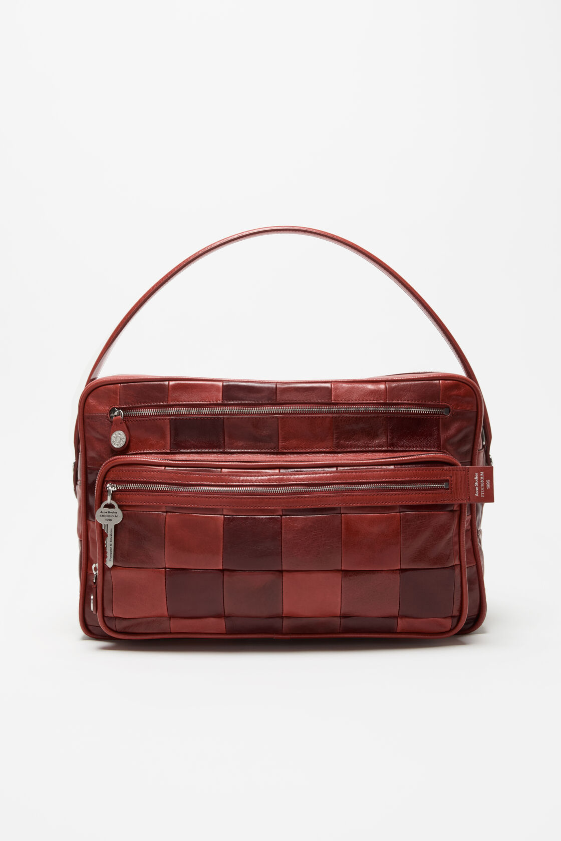 Acne Studios Camero Camera Patchwork Bag Bag in burgundy leather with woven square panels, two zip compartments, and a branded key charm.