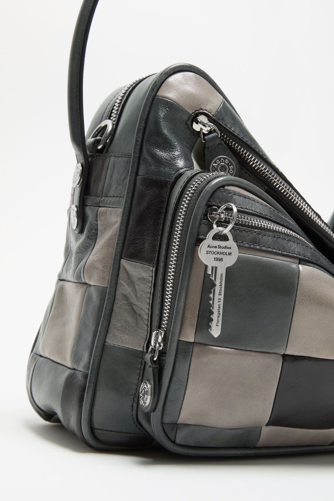 Close-up of an Acne Studios dark grey leather zipper with two branded silver-tone pull tabs embossed with the Acne Studios logo.