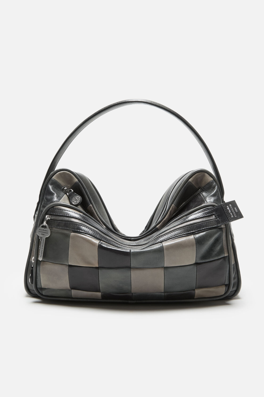 Acne Studios Camero Camera Patchwork Bag Bag in dark grey leather with checkerboard panels, zip compartments, a key charm, and a top handle.