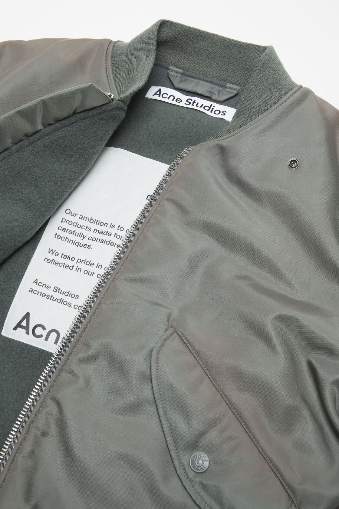Close-up of an Acne Studios stone grey washed bomber jacket in recycled nylon, with ribbed collar, front zip, and fleece lining.