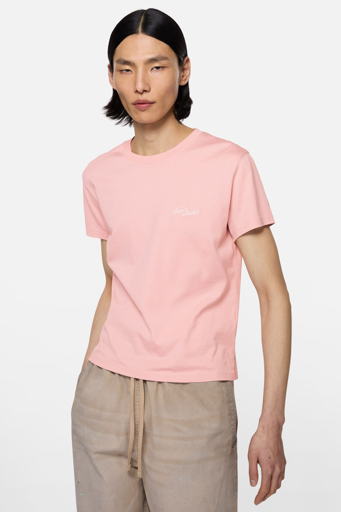Acne Studios fitted faded pink cotton jersey t-shirt with embroidered chest logo, worn with light beige drawstring trousers.