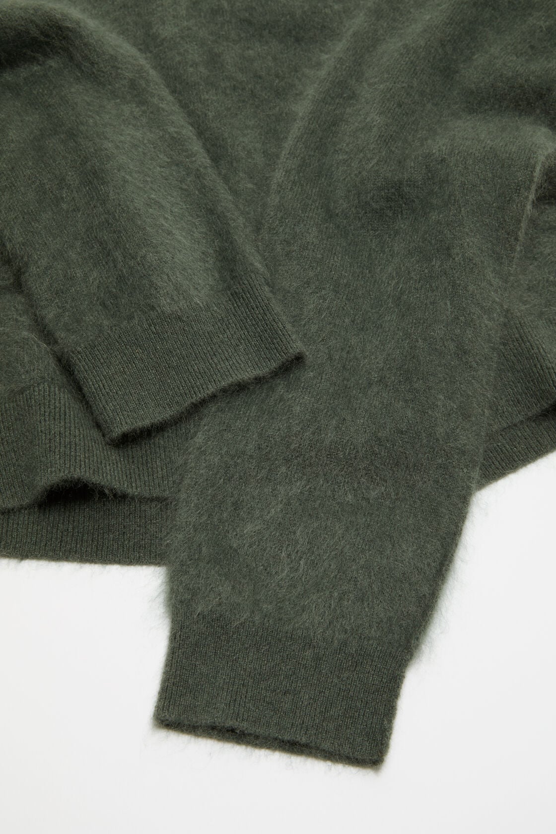 Close-up of an Acne Studios dark green cashmere v-neck sweater, showing the fluffy knit texture and ribbed cuffs.
