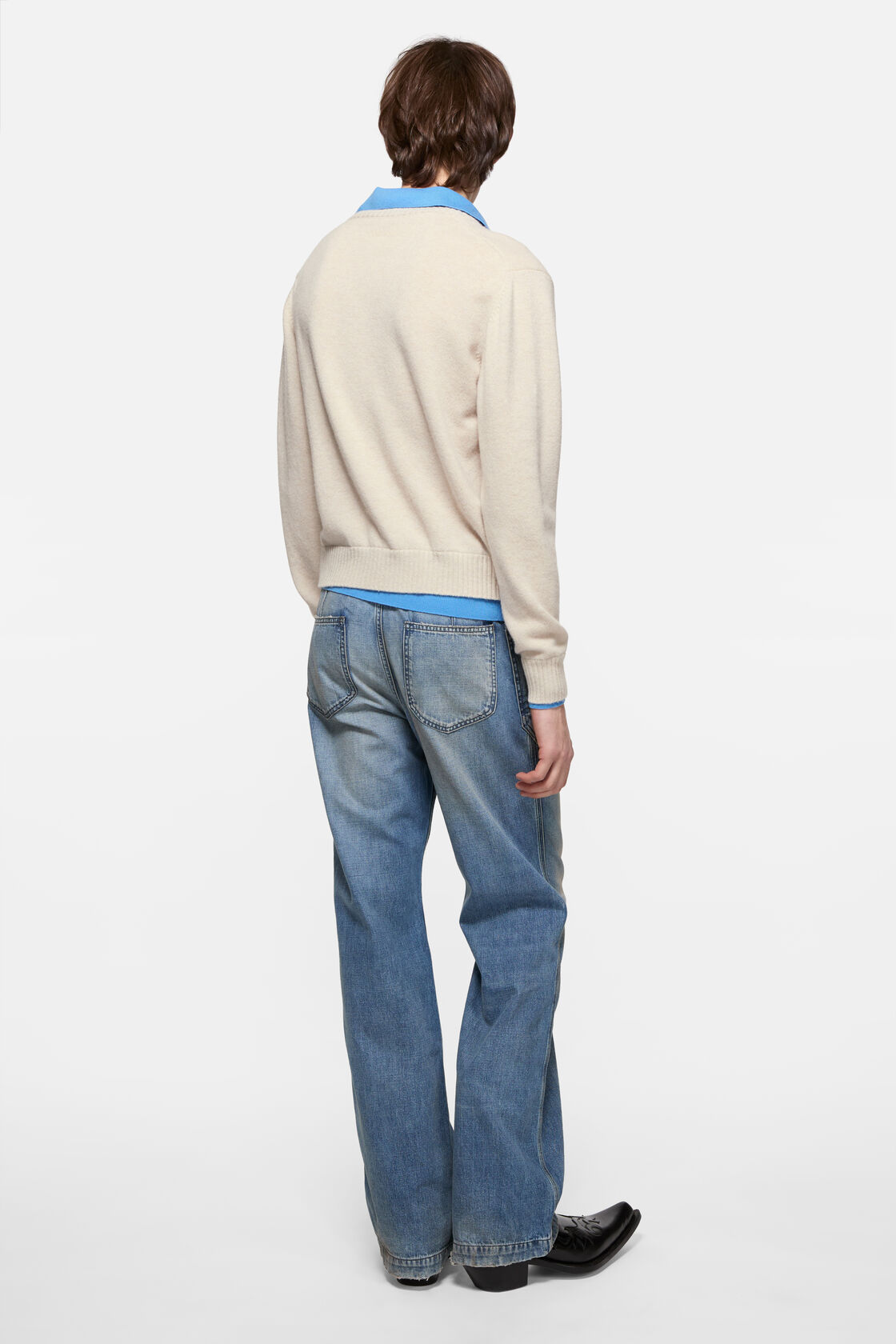 Acne Studios dirty white wool knit sweater with V-neck, layered over a blue polo shirt, styled with light-wash wide-leg jeans and black leather shoes.