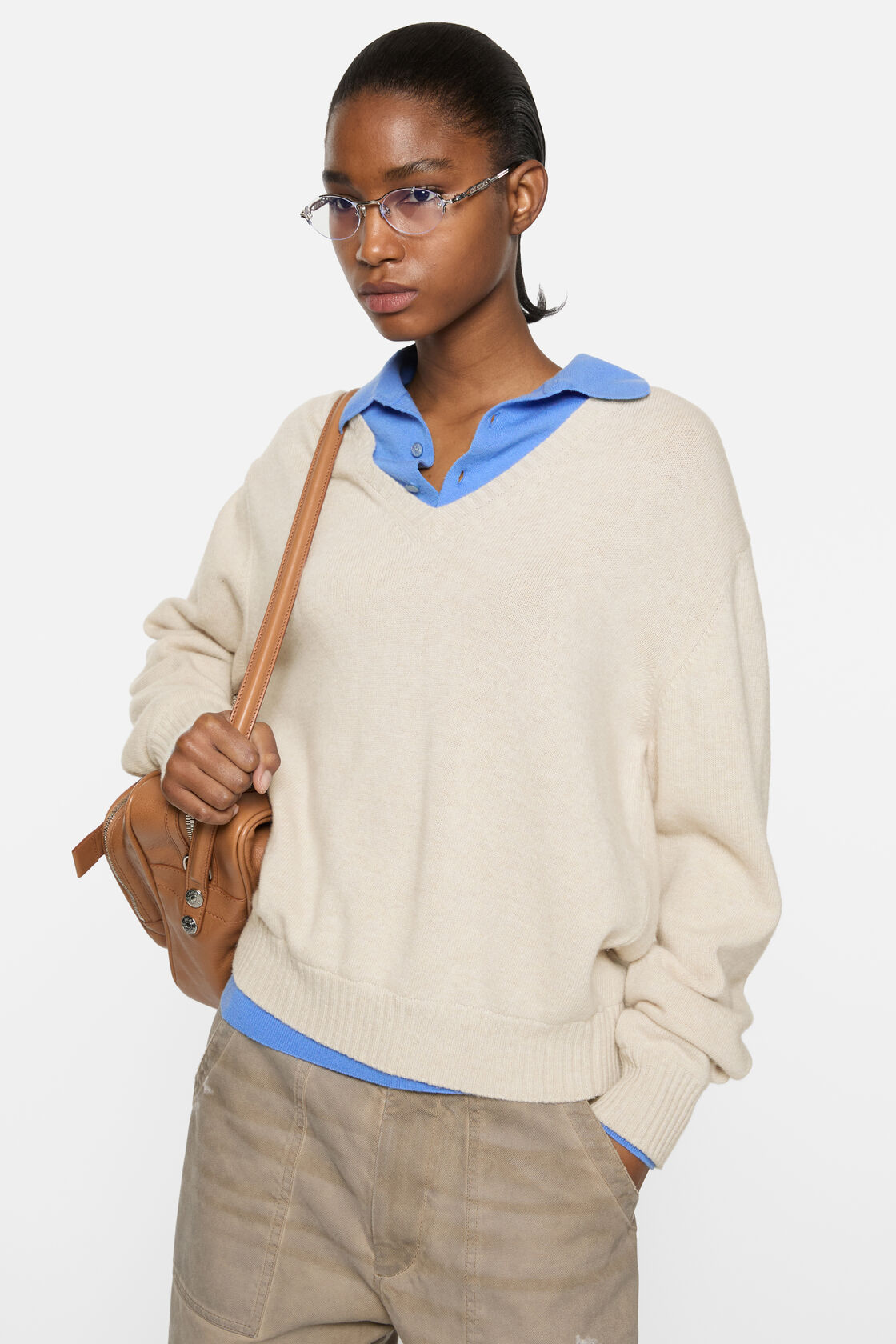Acne Studios dirty white wool V-neck sweater with relaxed fit, layered over a blue polo shirt, styled with khaki trousers and a tan leather shoulder