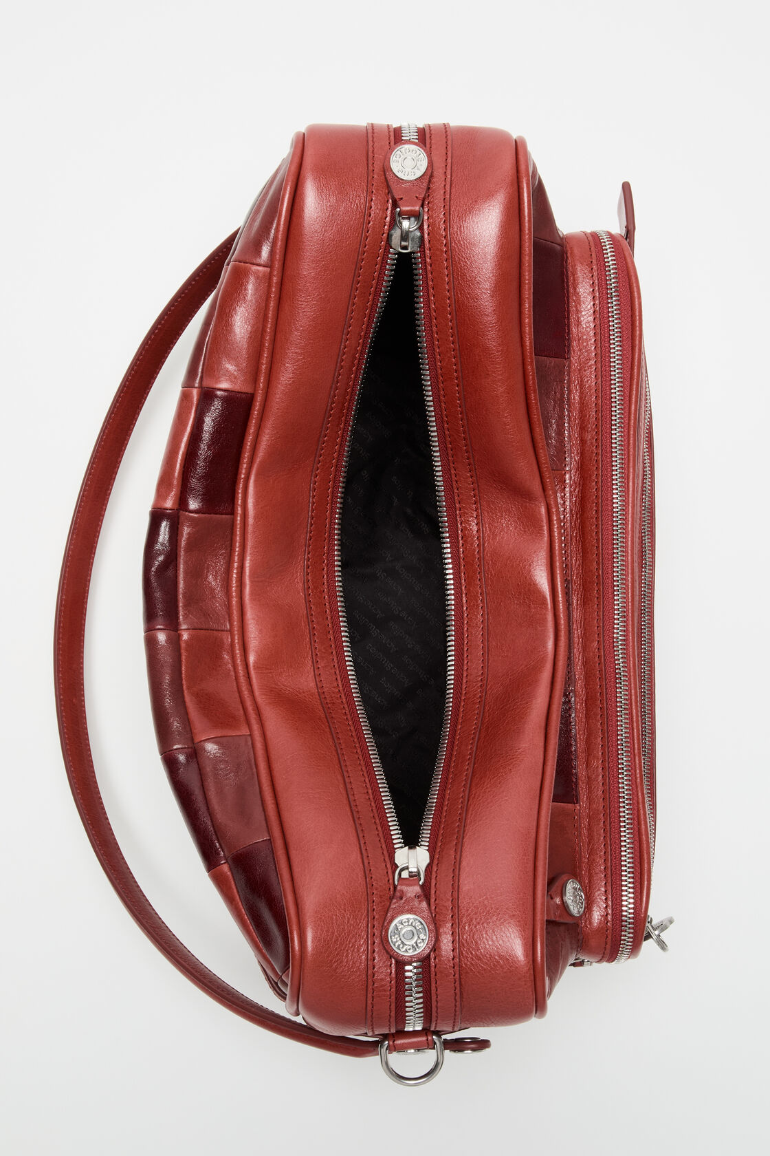 Close-up of an Acne Studios burgundy leather patchwork camera bag, showing woven leather panels, two branded silver snap buttons, and a top handle.