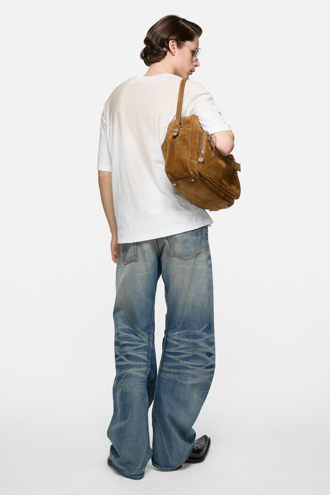 Acne Studios dusty white sprayed logo t-shirt worn from behind, styled with wide-leg faded blue jeans and a tan suede shoulder bag.