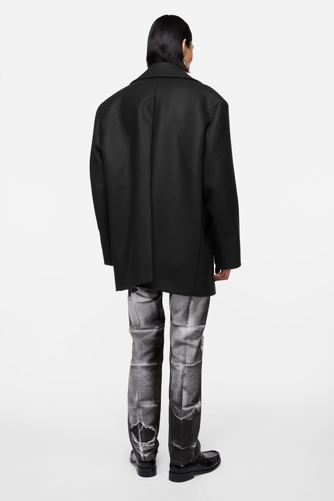 Acne Studios black wool peacoat with boxy silhouette, shown from the back, worn with grey distressed jeans and black boots.