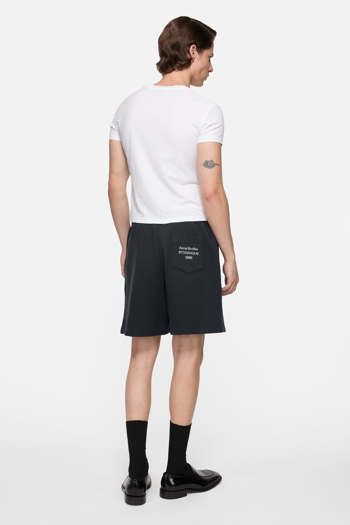Acne Studios off-white logo T-shirt worn from the back, styled with black flared leather trousers and a brown leopard-print shoulder bag.
