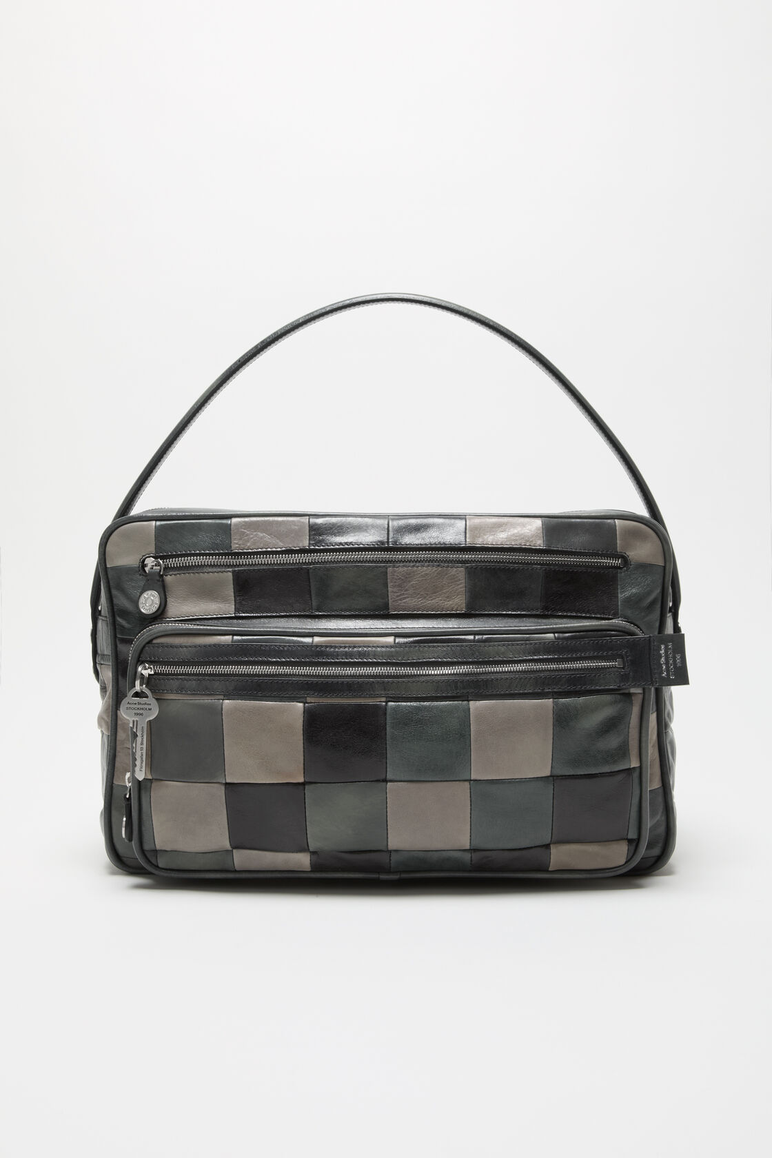 Acne Studios Camero Camera Patchwork Bag Bag in dark grey leather with checkerboard panels, two zip compartments, branded key charm, and a top handle.