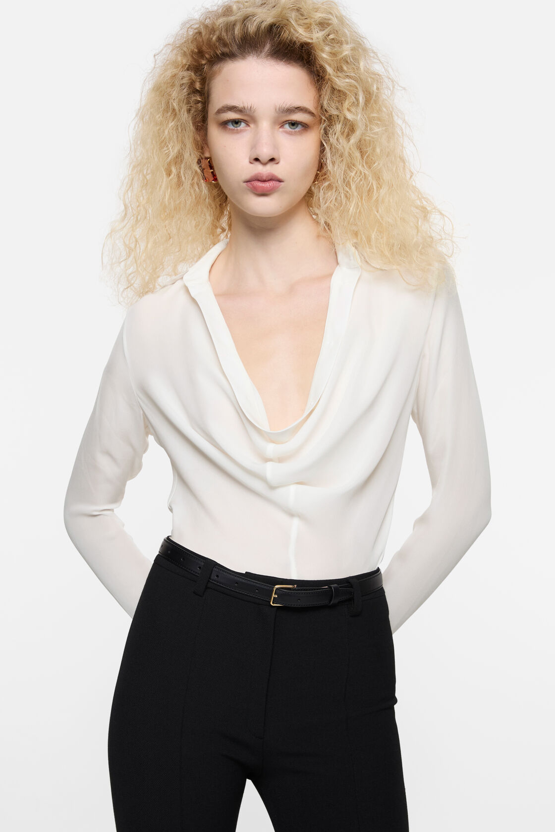 Acne Studios white silk cowl-neck blouse with long sleeves, worn with black trousers and black leather belt with gold buckle.