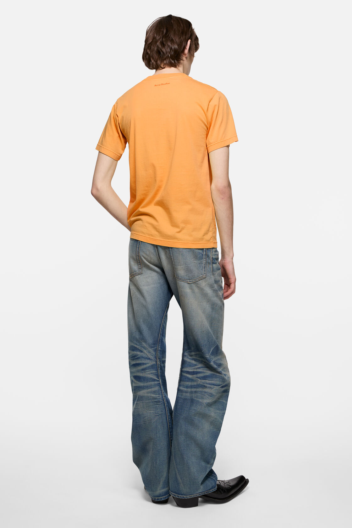 Acne Studios saffron yellow sprayed graphic t-shirt in cotton jersey, crewneck, regular fit, worn with light blue wide-leg jeans and black boots.