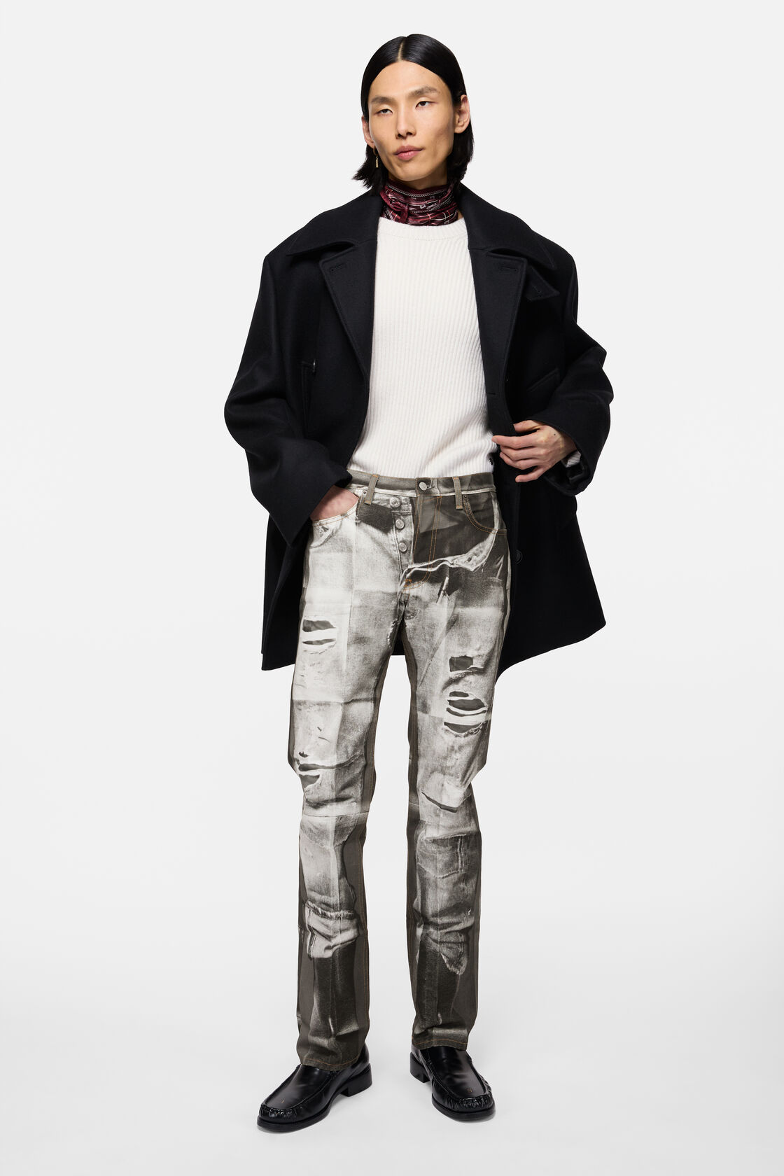 블랙 앤 화이트 디스트레스드 프린트의 Acne Studios 트롱프뢰유 스트레이트 레그 진. 블랙 오버사이즈 코트, 화이트 립 니트, 레드 프린트 스카프와 함께 착용.