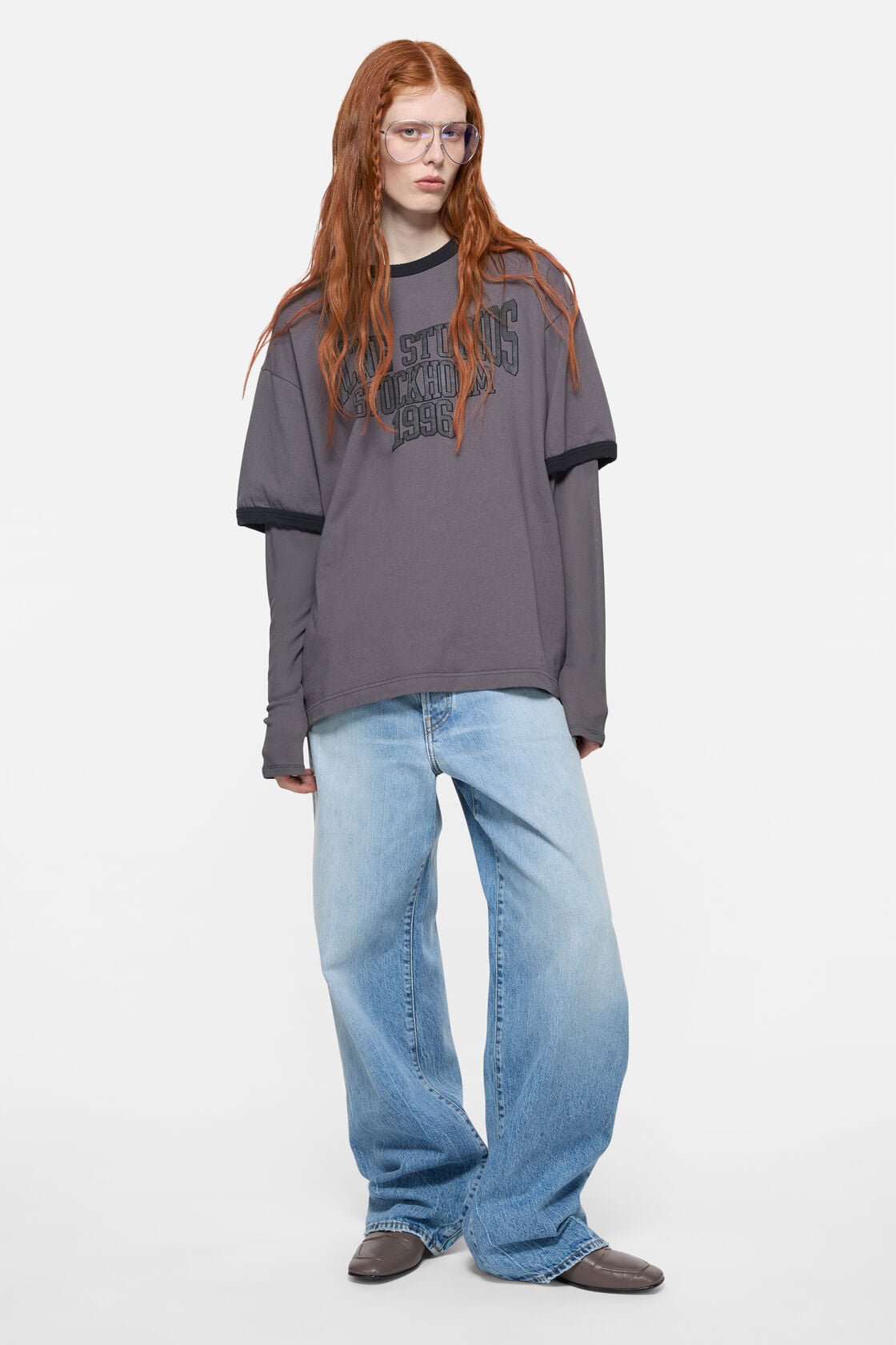 Acne Studios 1981 loose fit light blue wide-leg washed denim jeans, styled with a grey graphic T-shirt and grey ankle boots.