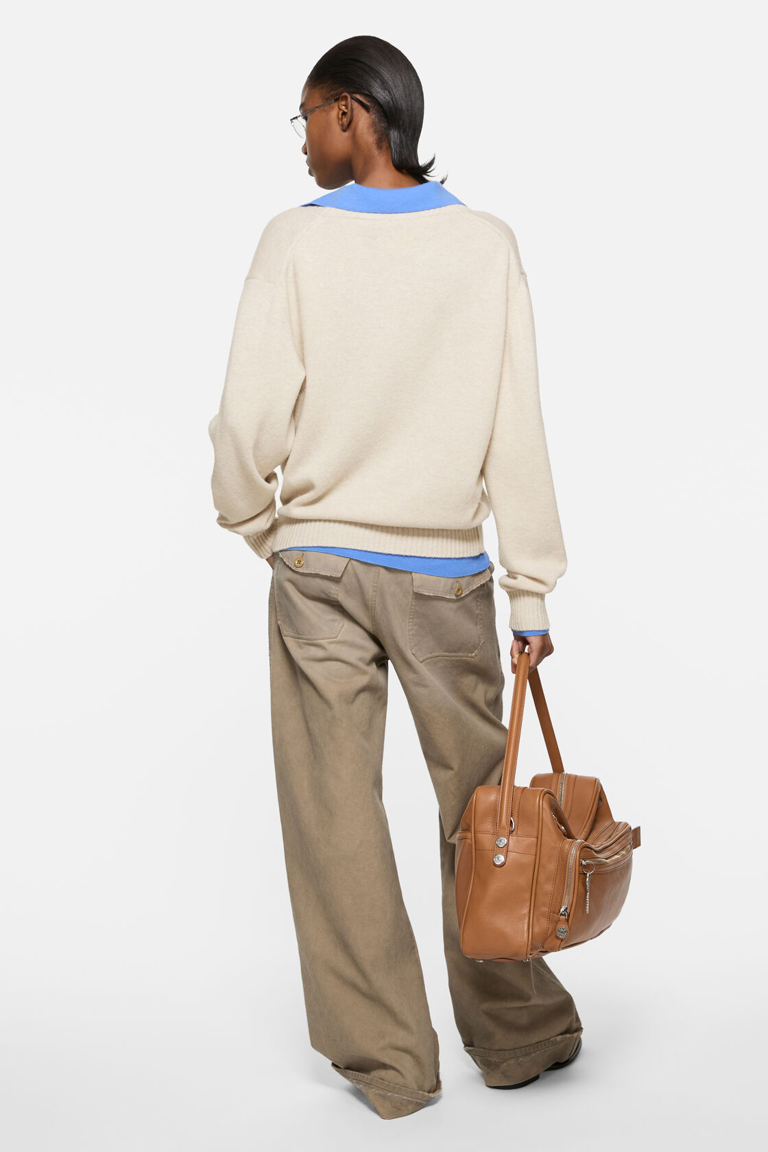 Acne Studios dirty white wool knit sweater with V-neck, layered over a blue polo top, styled with wide-leg khaki trousers and a tan leather bag.
