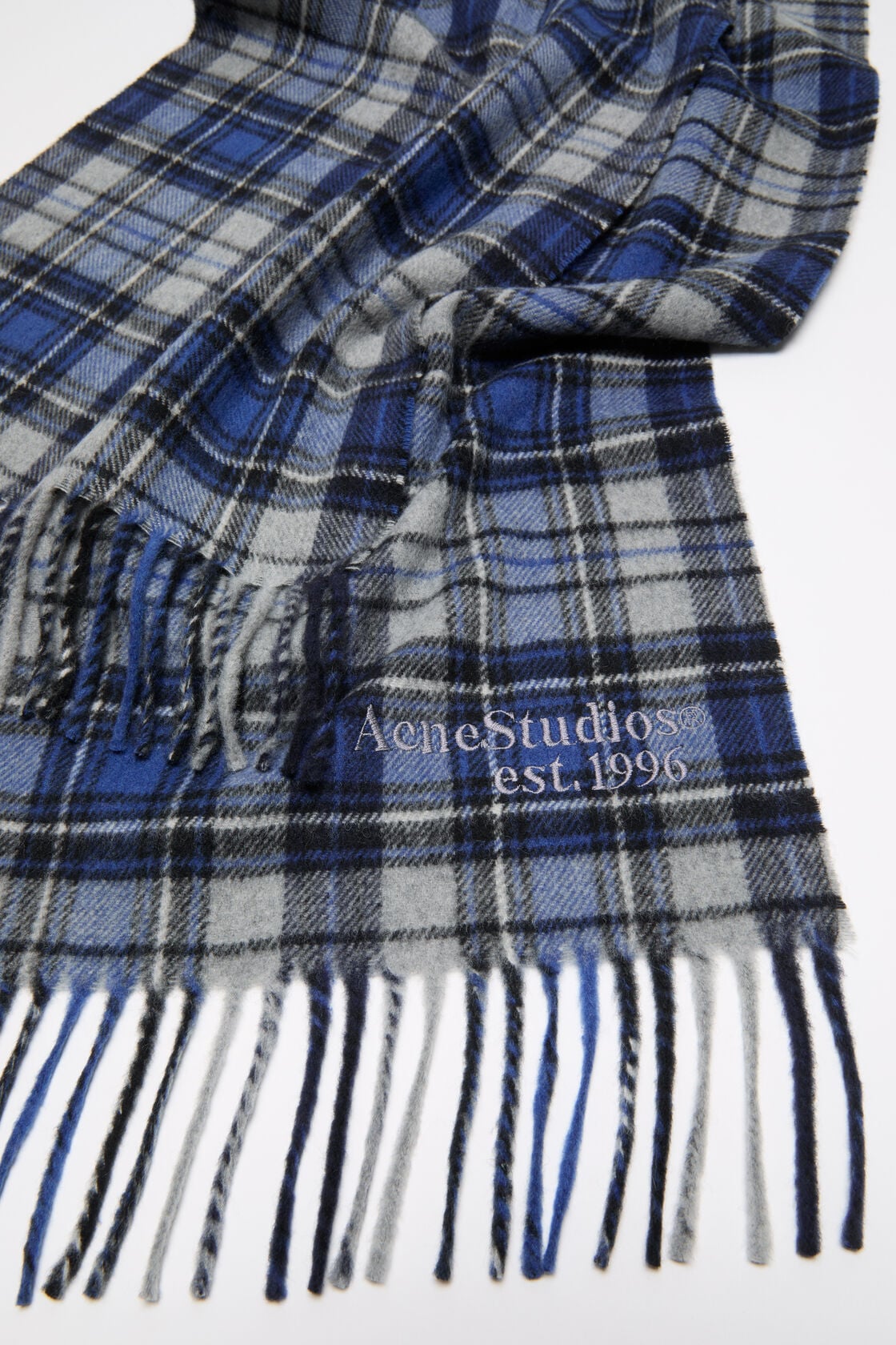 Close-up of an Acne Studios blue and grey tartan cashmere scarf with fringe ends and an embroidered logo.