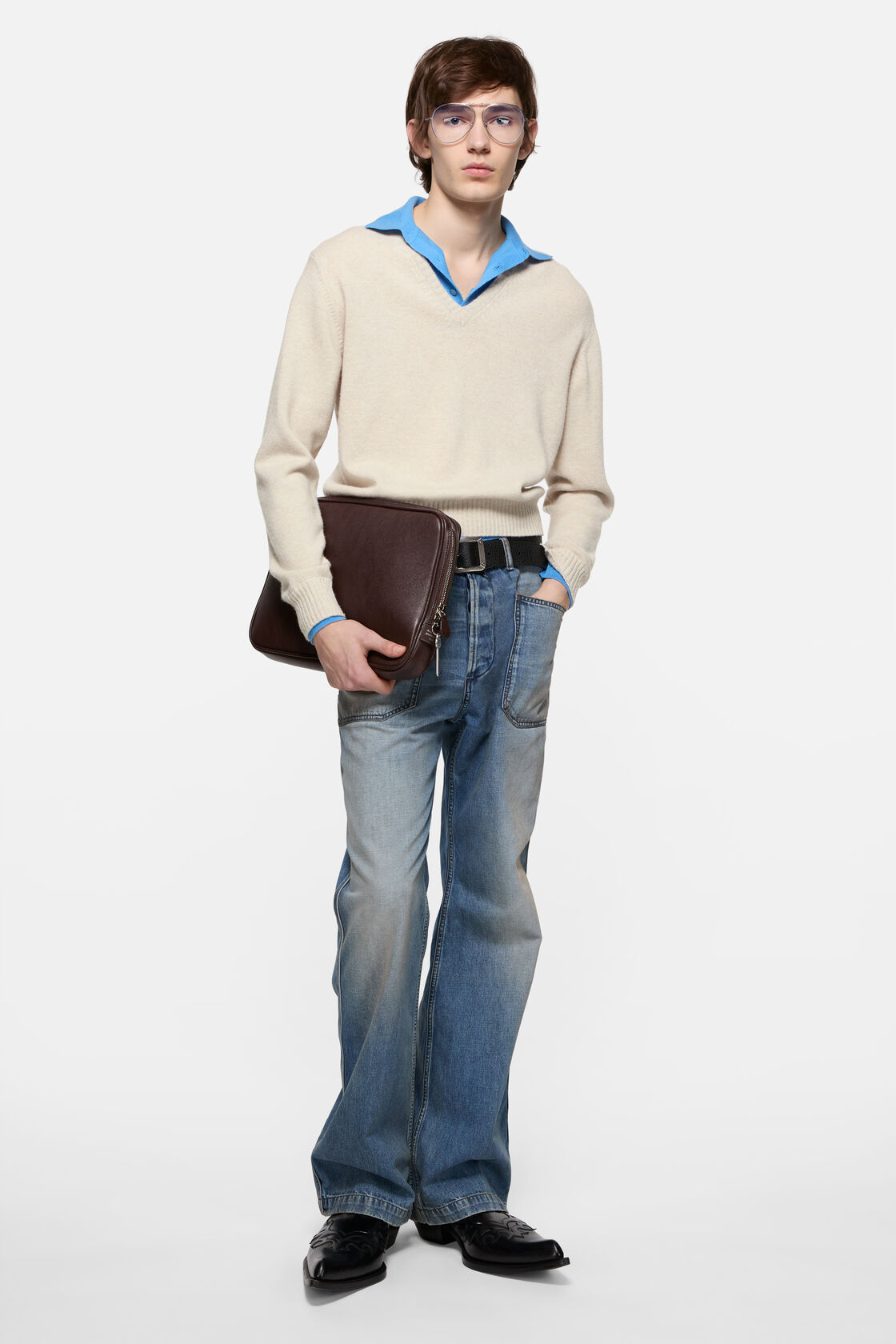 Acne Studios dirty white wool V-neck knit sweater in relaxed fit, layered over a blue polo shirt, styled with light-wash flared jeans, a black belt,