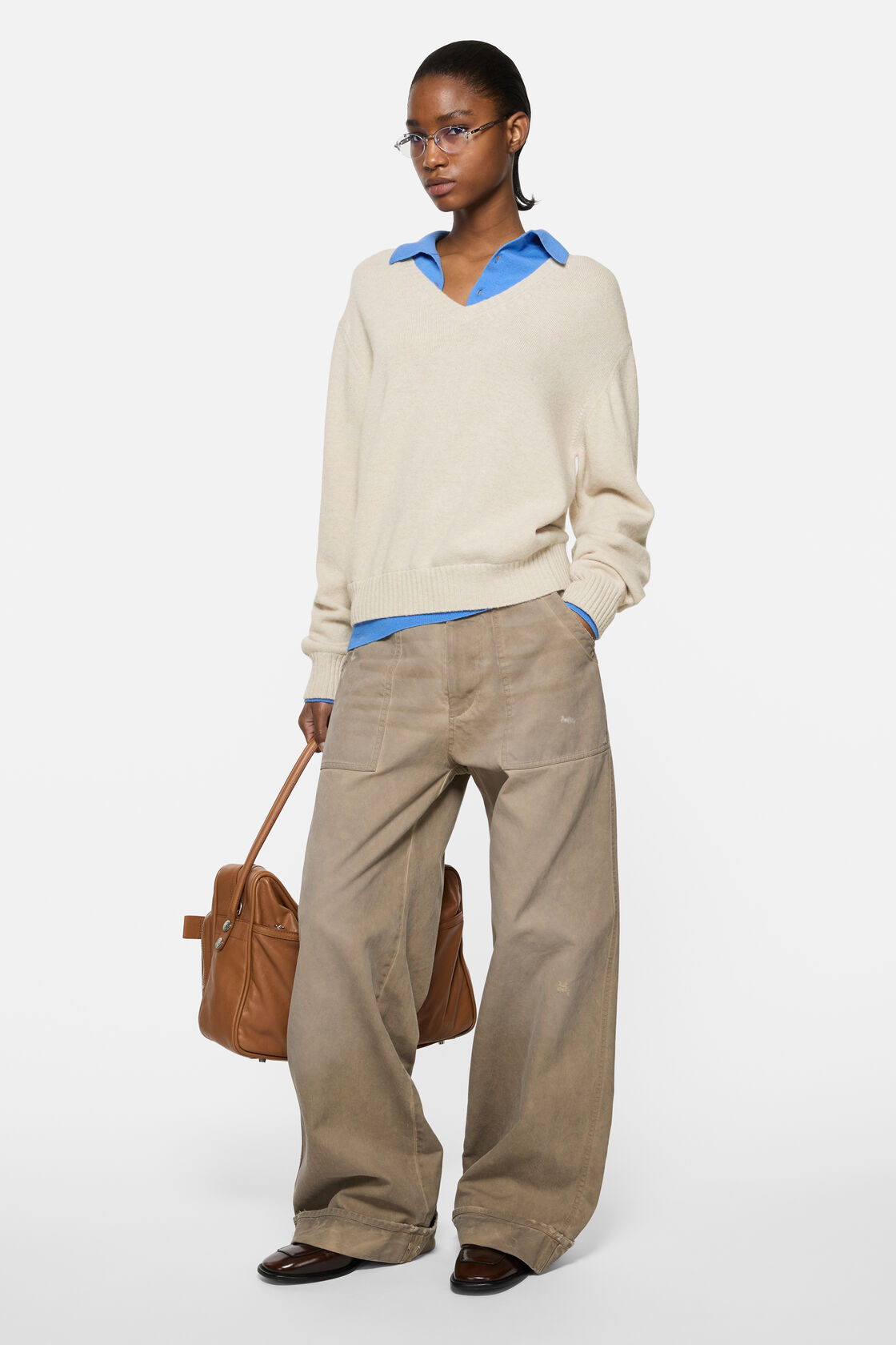 Acne Studios dirty white wool V-neck knit sweater with relaxed fit, layered over a blue polo shirt, styled with wide-leg khaki trousers, brown
