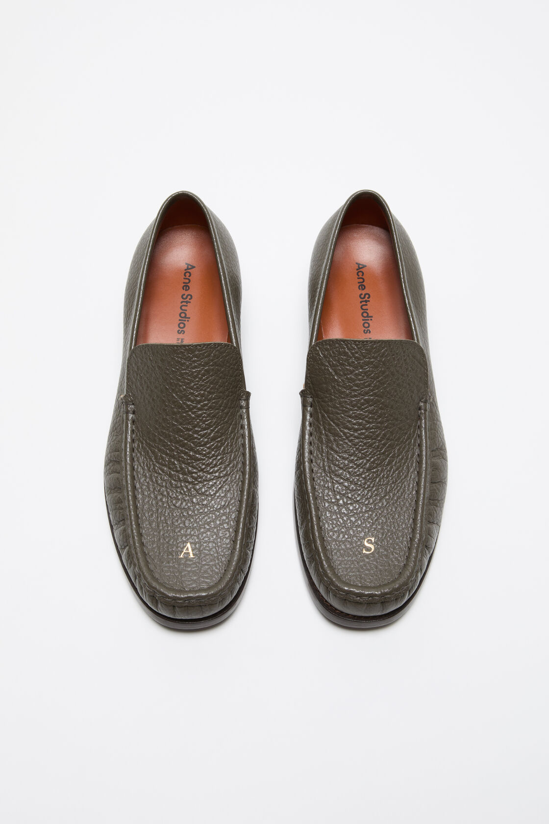 Acne Studios khaki green grained leather loafers with gold debossed initials on the toe and tan leather insole.