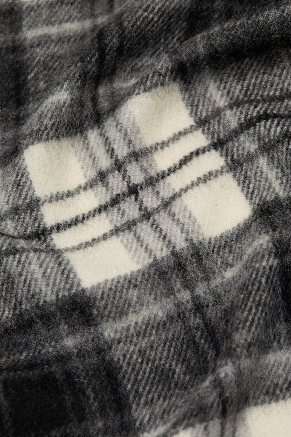 Close-up of an Acne Studios black and white cashmere scarf showing a large-scale check pattern on a soft, brushed wool-like fabric.