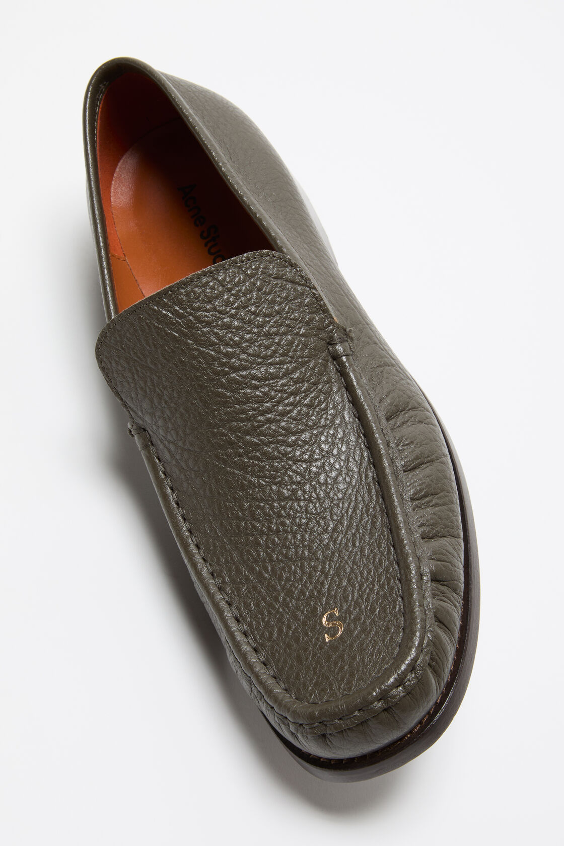 Acne Studios khaki green pebbled leather loafer with moccasin stitching, gold embossed logo, and a tan leather insole.