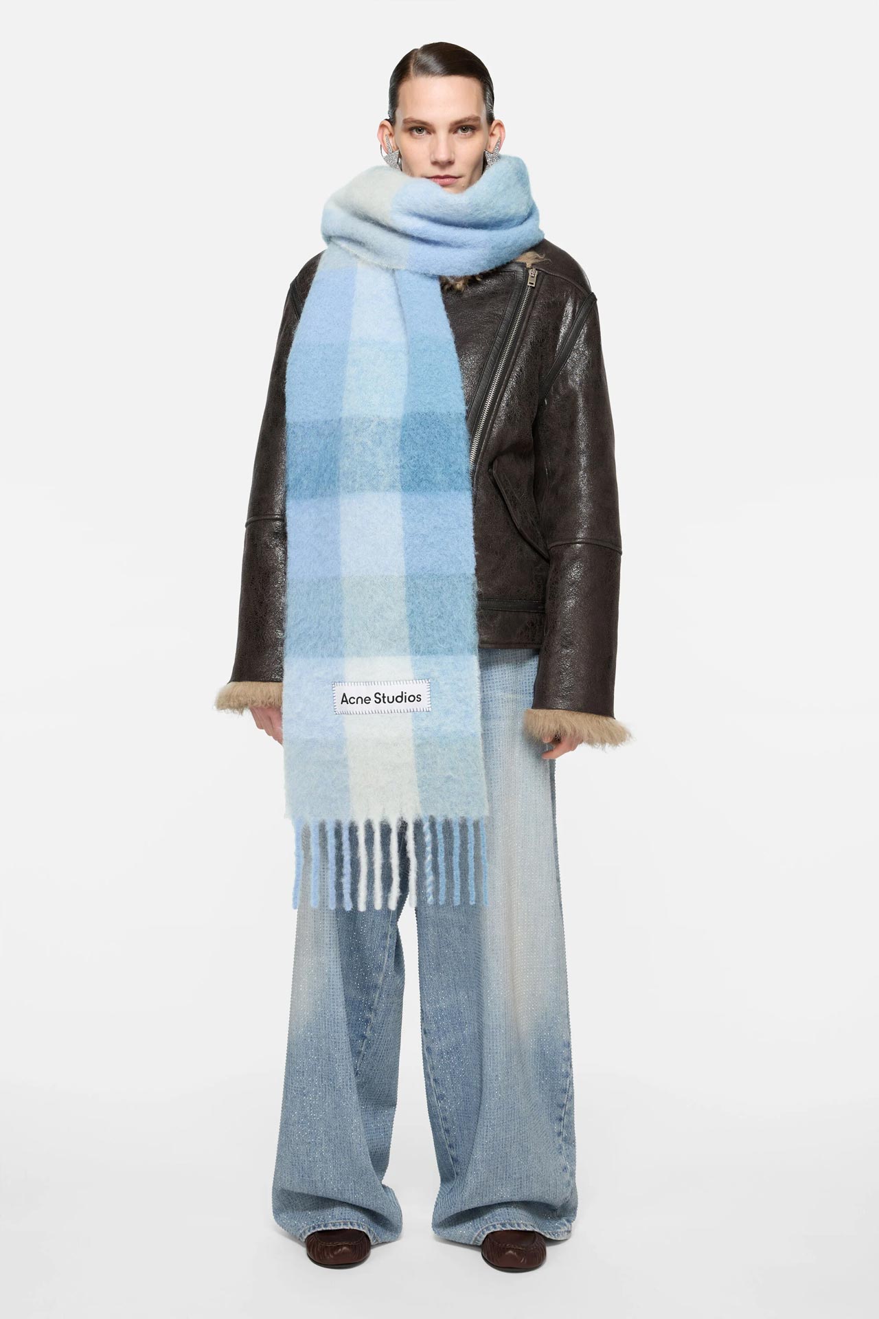 Female model wearing Vally mohair mix light blue checked scarf by Acne Studios, blue jeans and brown leather jacket.