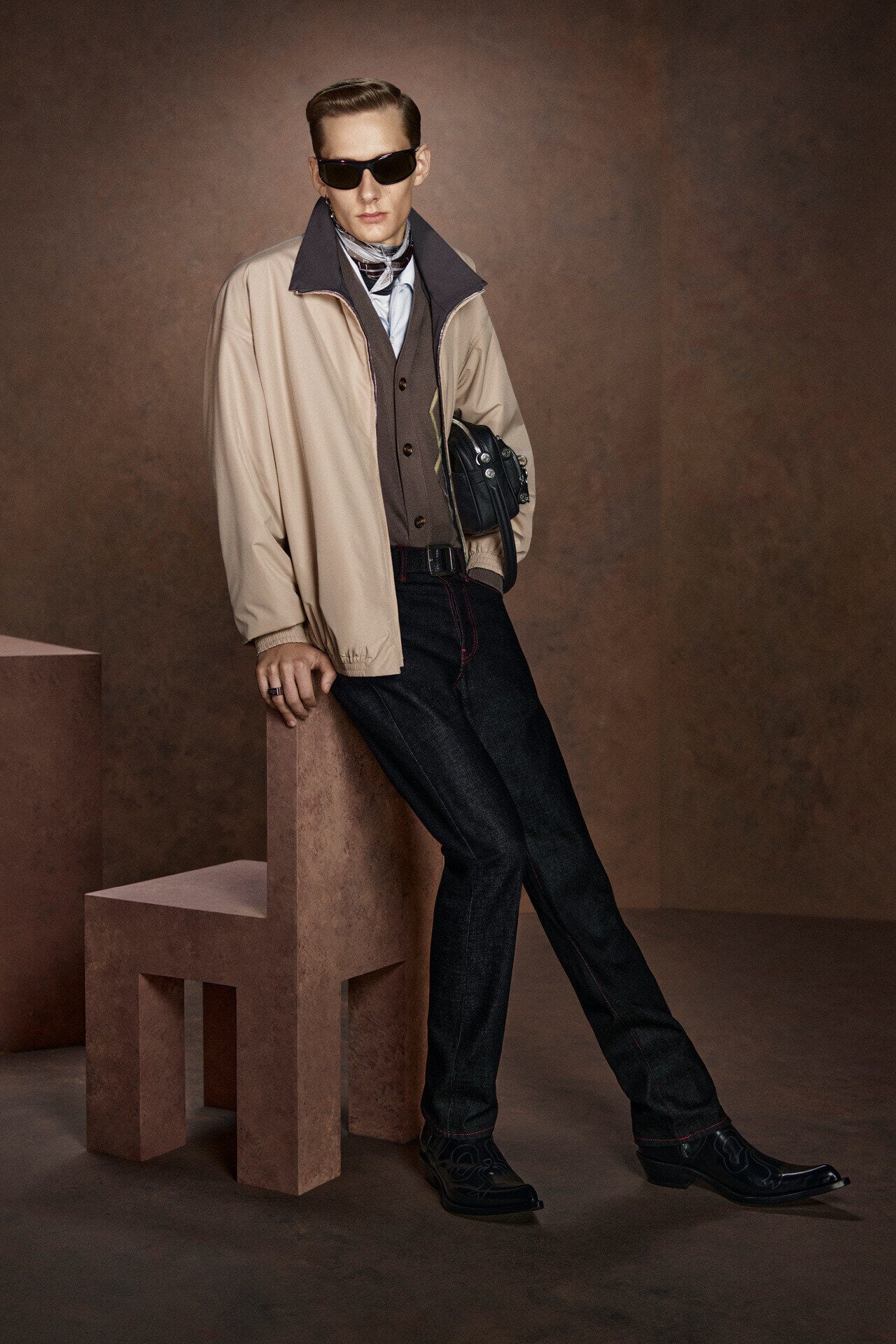 Acne Studios beige bomber jacket and dark jeans, black sunglasses.