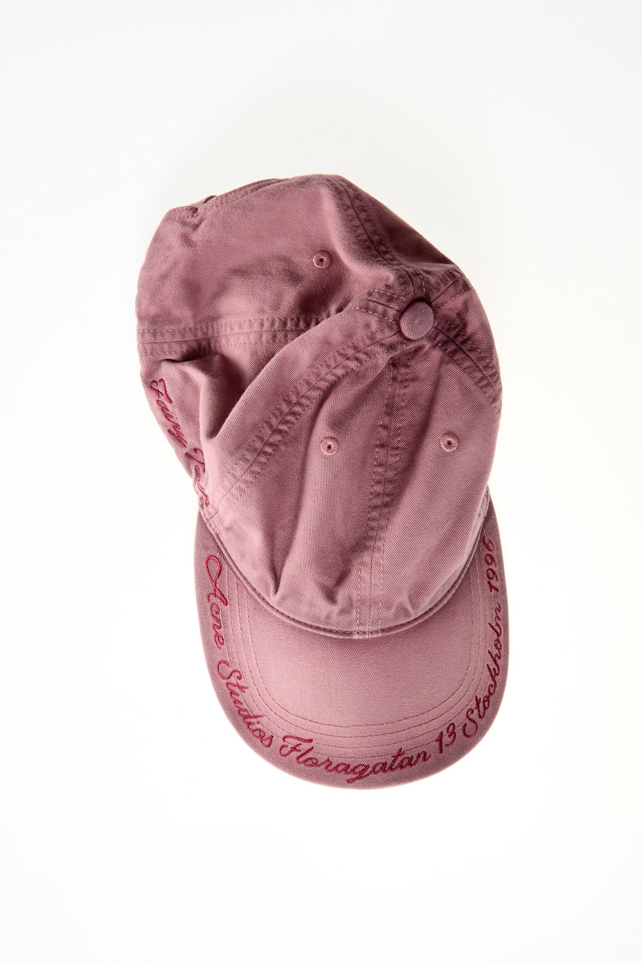A creative product image of the Acne Studios faded pink cap with text details.