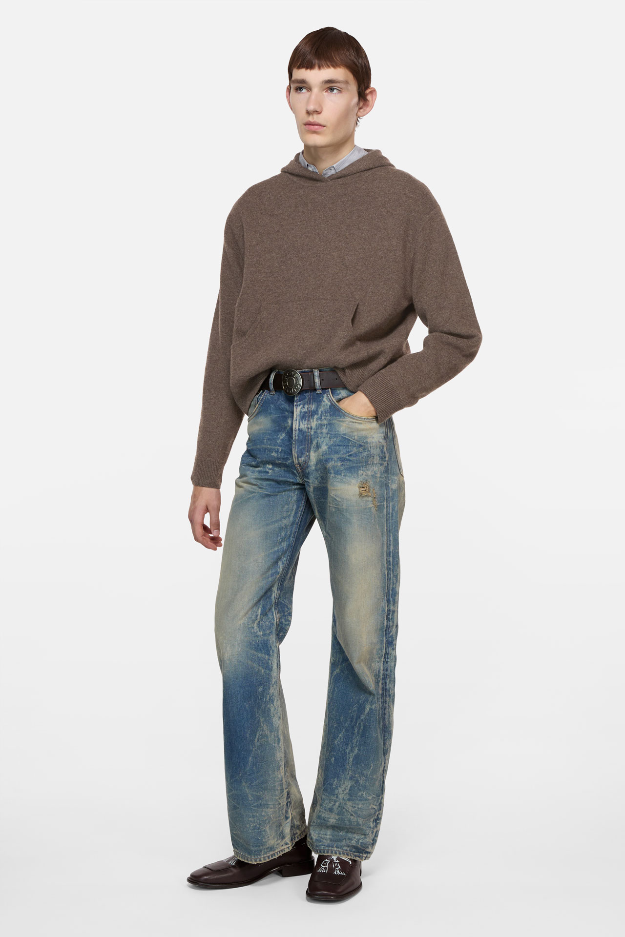 A male model wearing a brown cashmere hooded sweater, blue jeans and brown leather loafers and belt.
