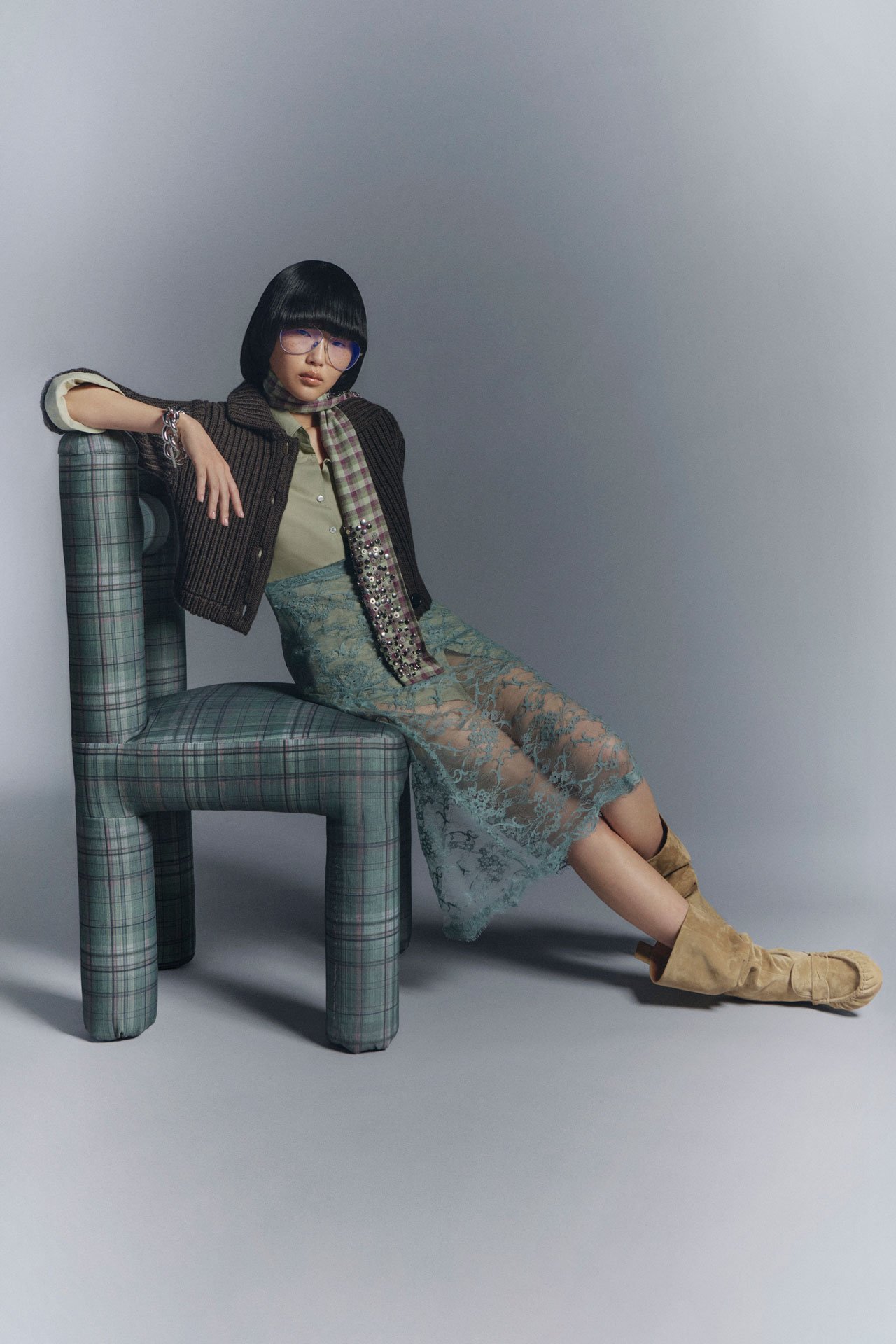 Female model wearing a a purple flower-print shirt and green flower-print skirt, having a brown suede Camero bag on her shoulder.