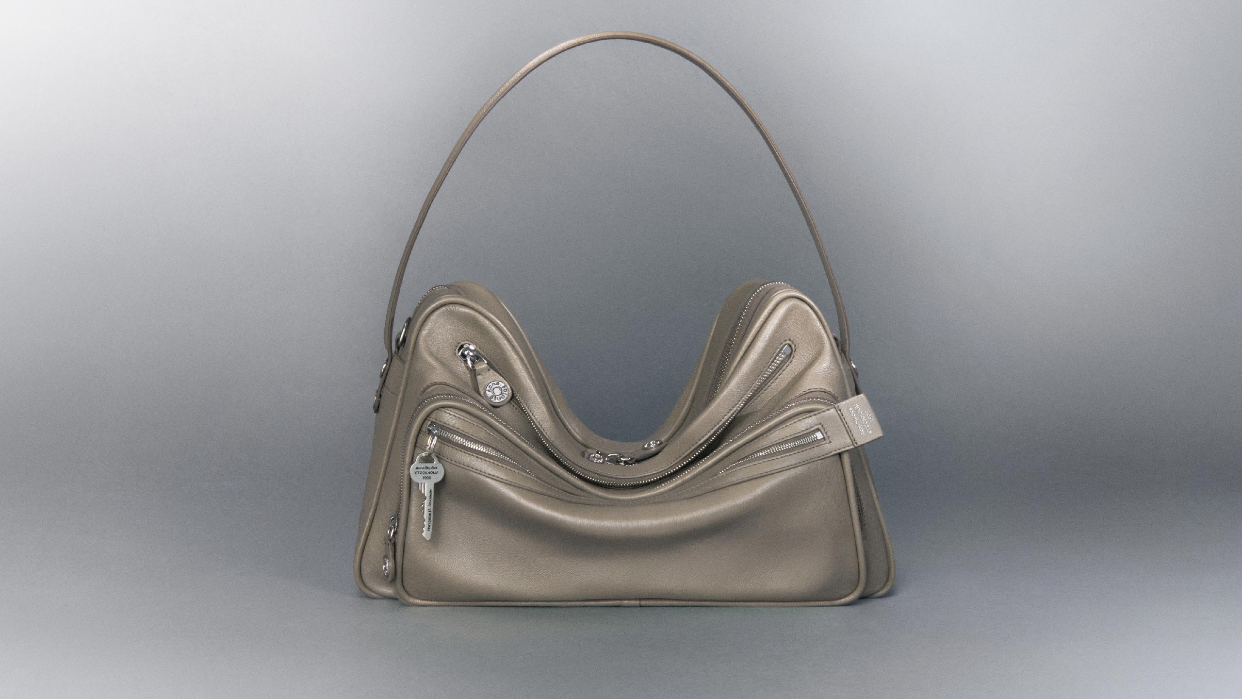 Acne Studios Camero Camera shoulder bag in taupe beige with grey background.