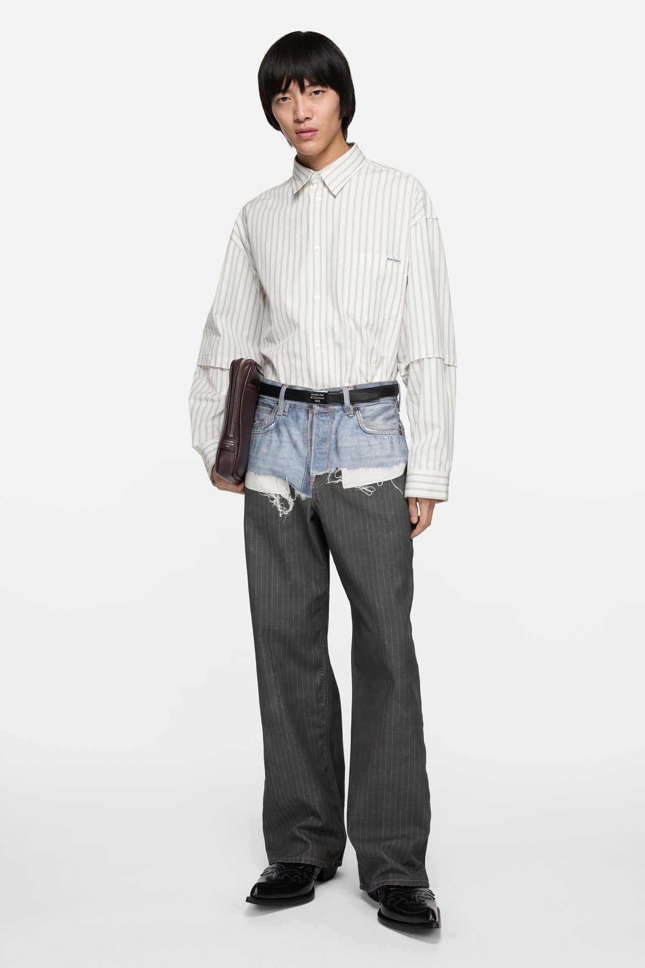 A male model wearing a white striped shirt, TLO grey-blue jeans and holding a brown leather laptop case.