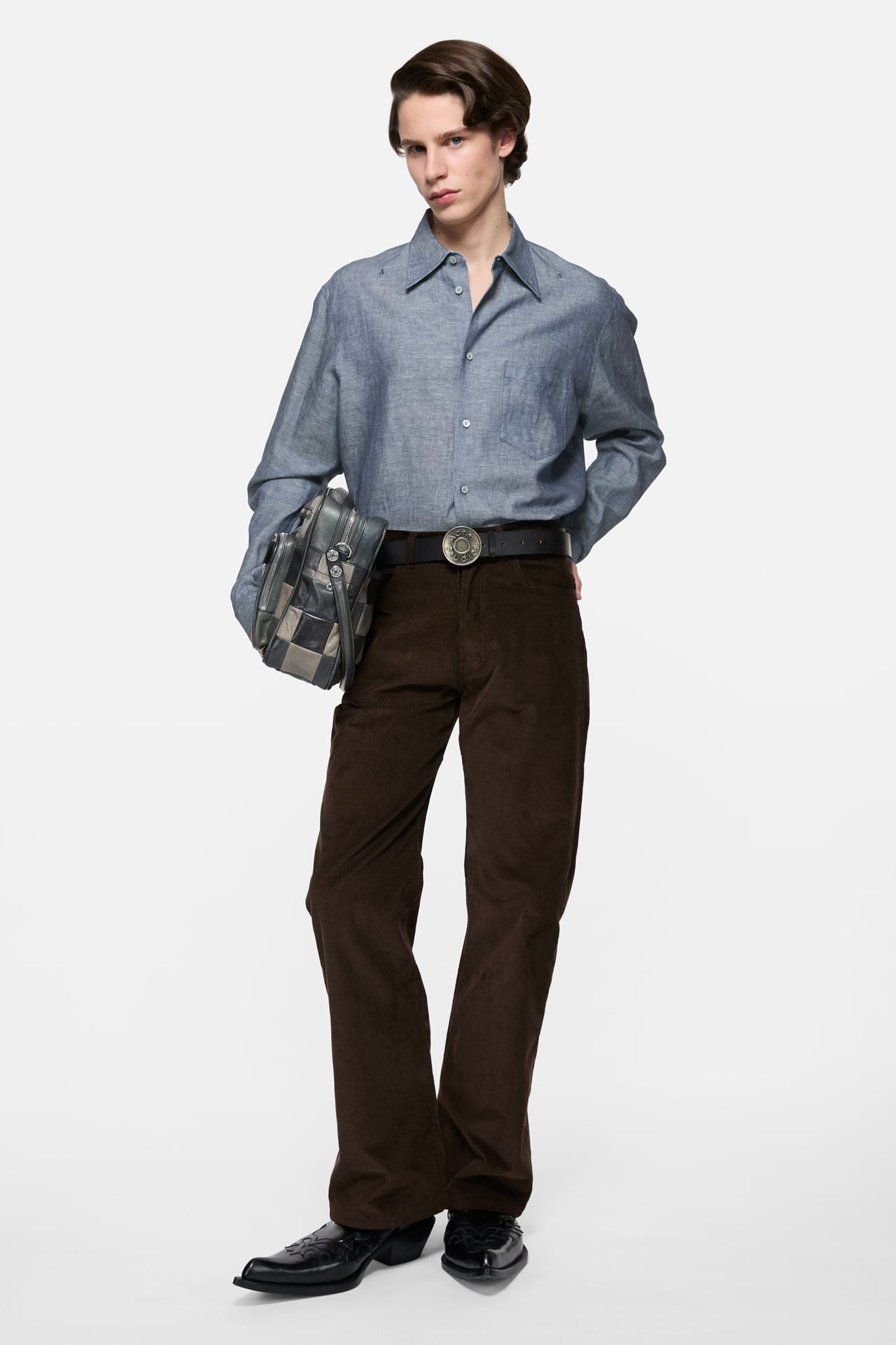 Acne Studios Menswear blue satin shirt, brown pants, black leather bucket belt and cowboy boots and a green leather Camero bag.
