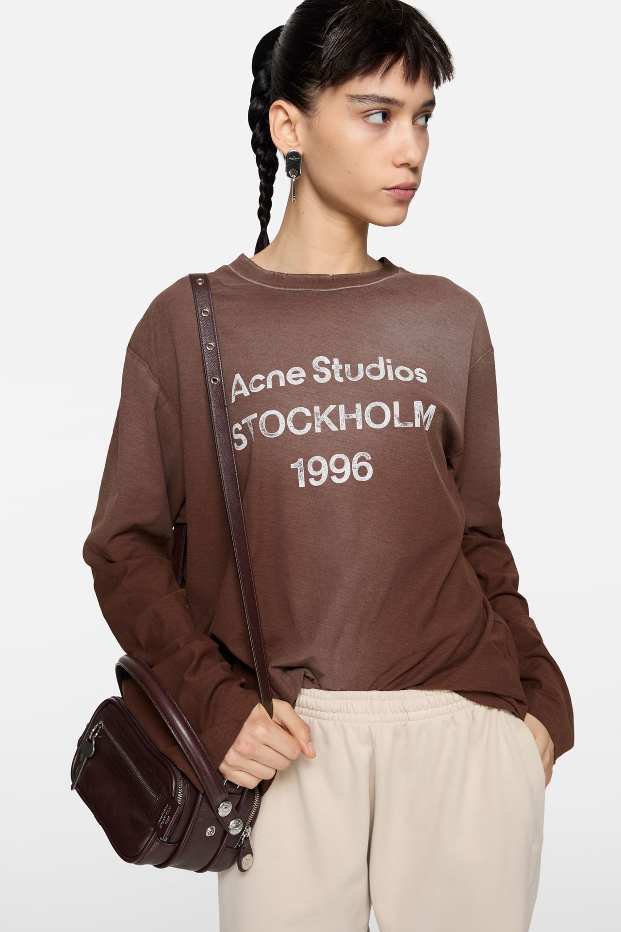 A female model wearing an Acne Studios 1996 logo brown long-sleeve t-shirt.