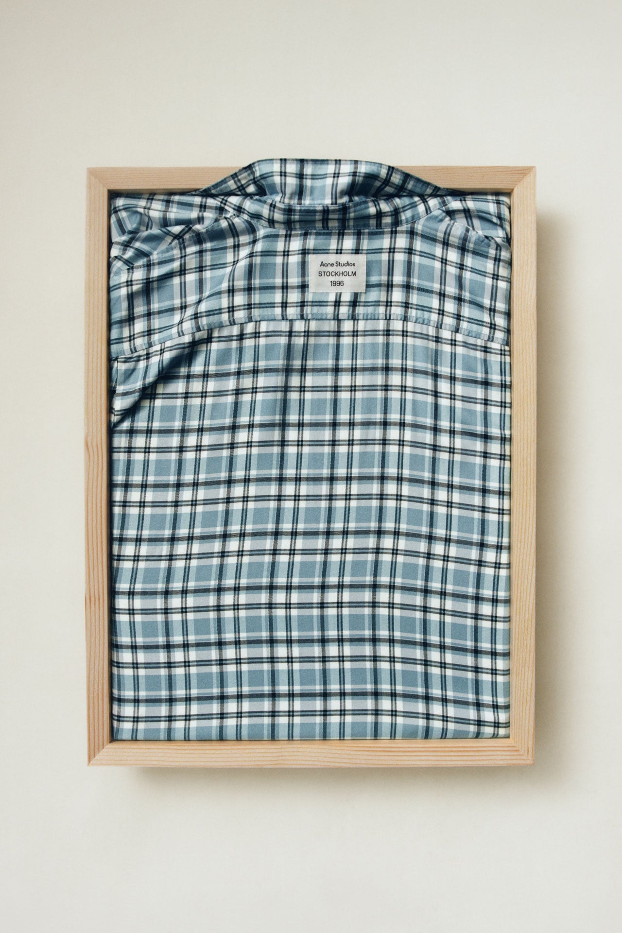 Acne Studios blue checked shirt folded and presented on a wooden tray.