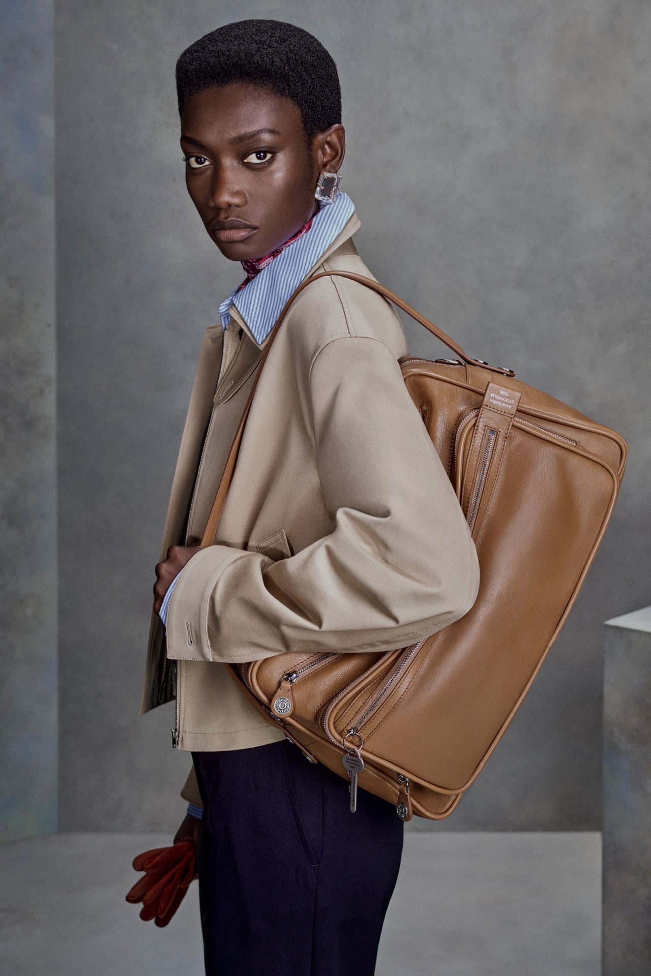 Acne Studios caramel brown leather Camero Camera bag, presented on a model wearing beige jacket and navy blue pants.