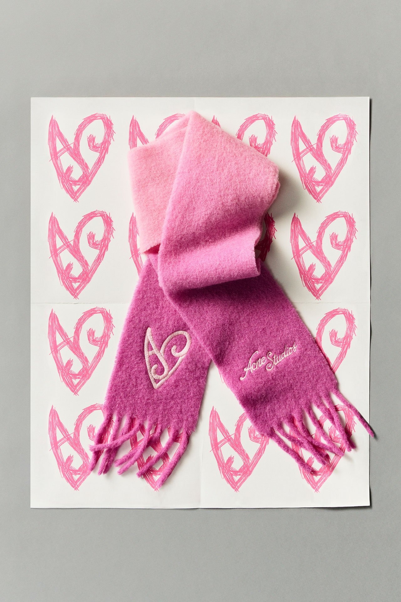 Acne Studios SS26 Year of the Horse pink scarf with a heart detail, laying on white paper with pink hearts on it.