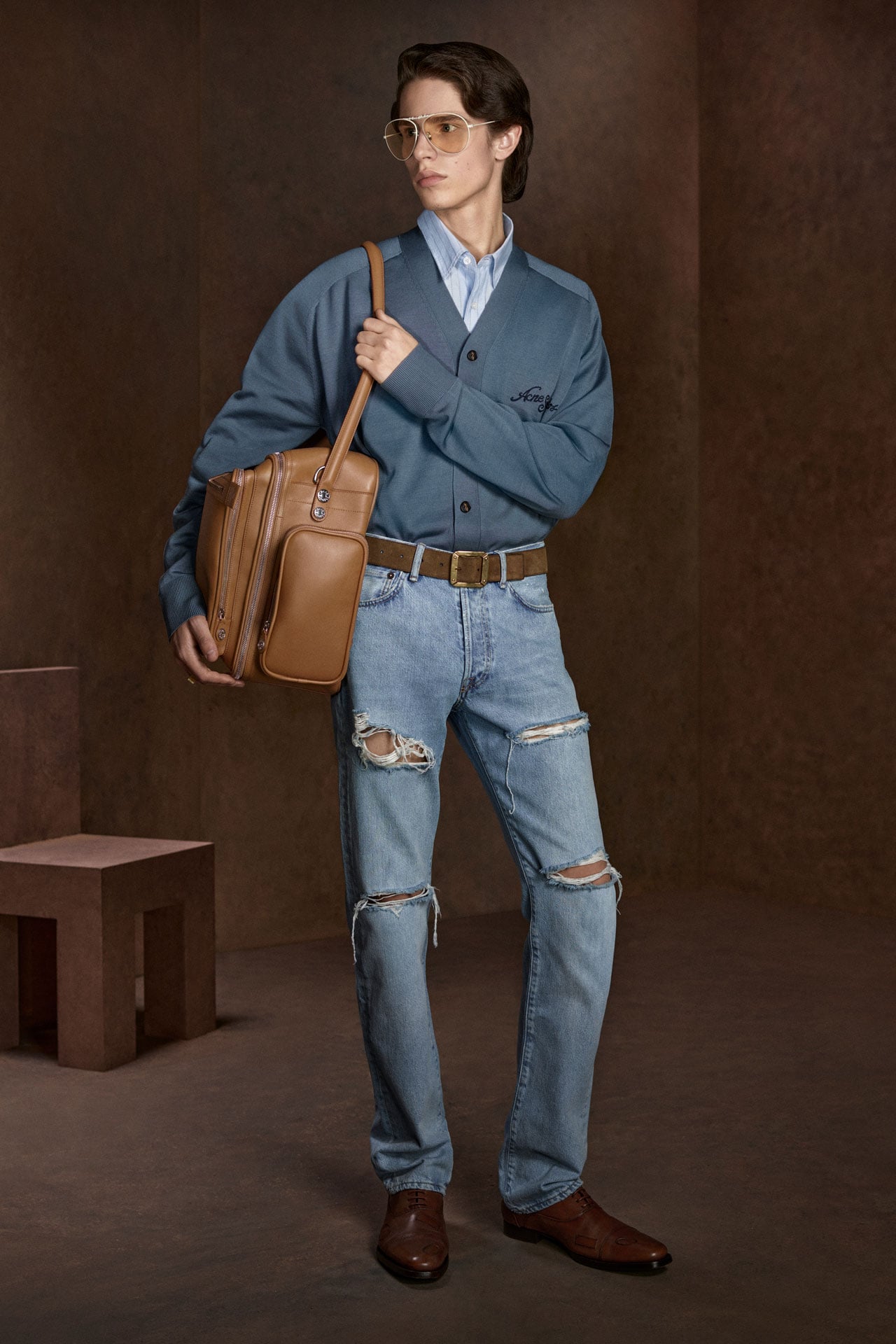 Acne Studios SS27 Mens Collection - light blue ripped straight jeans, blue knitted cardigan, brown belt and brown leather loafers, big brown leather Camero bag.