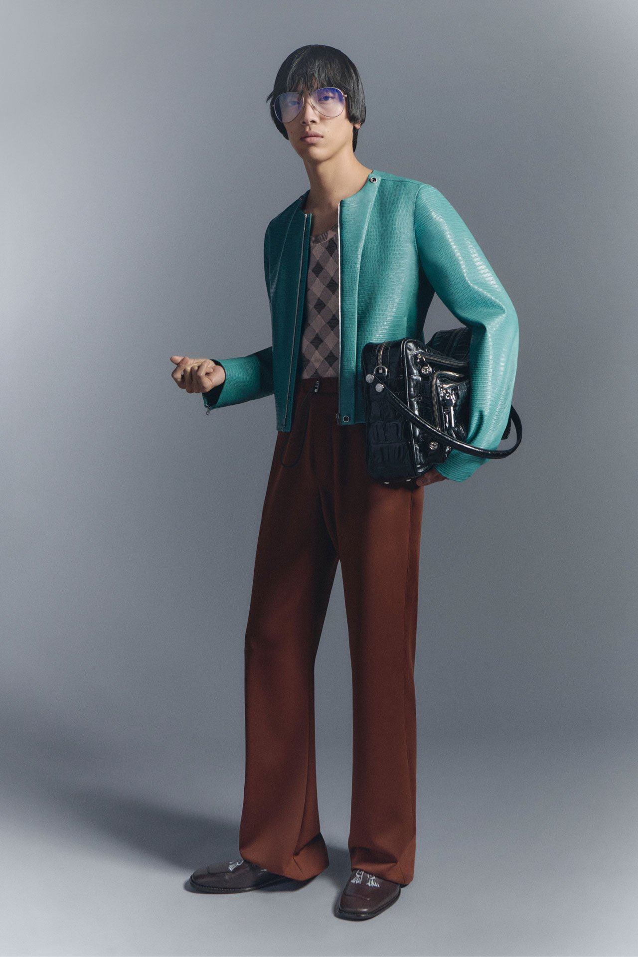 SS26 Acne Studios Mens New Arrivals - male model wearing bright blue leather jacket, checked shirt, brown pants and holding a black leather Camero bag.