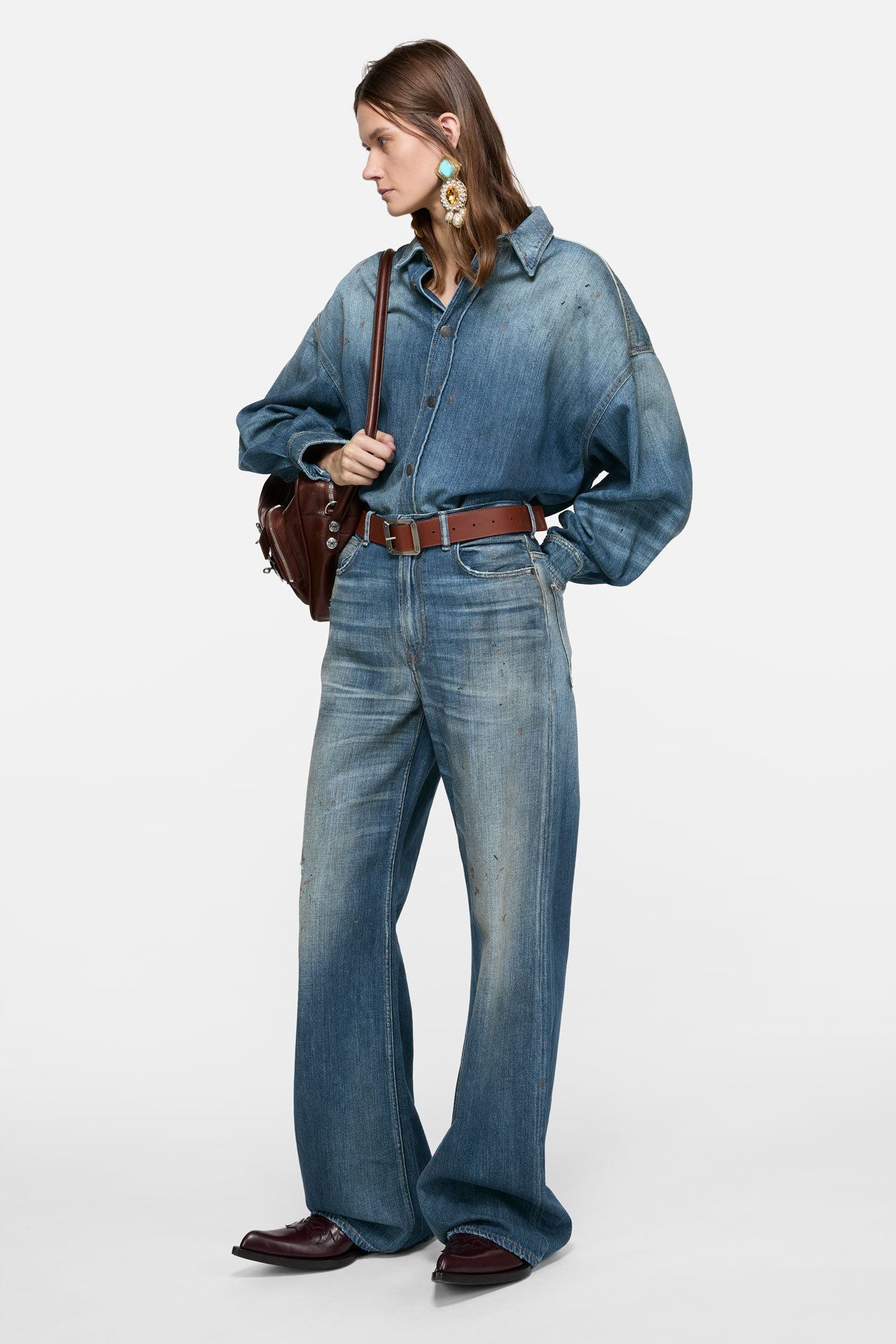 A female model wearing matching denim jeans and jackets, brown leather belt and Camero bag.