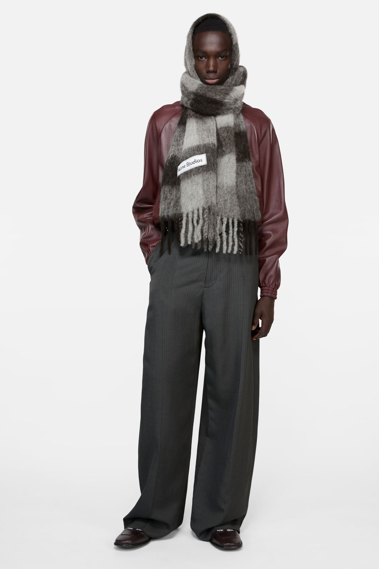 Female model wearing Vally mohair mix grey checked scarf by Acne Studios, vine-red bomber jacket and grey tailored pants.
